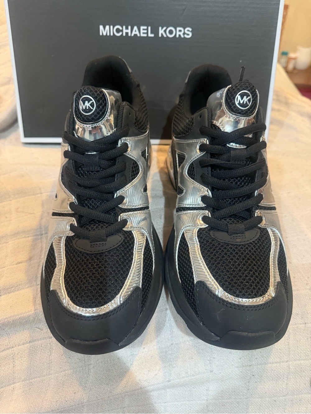 Michael Kors sneakers feature a black mesh upper with striking metallic silver